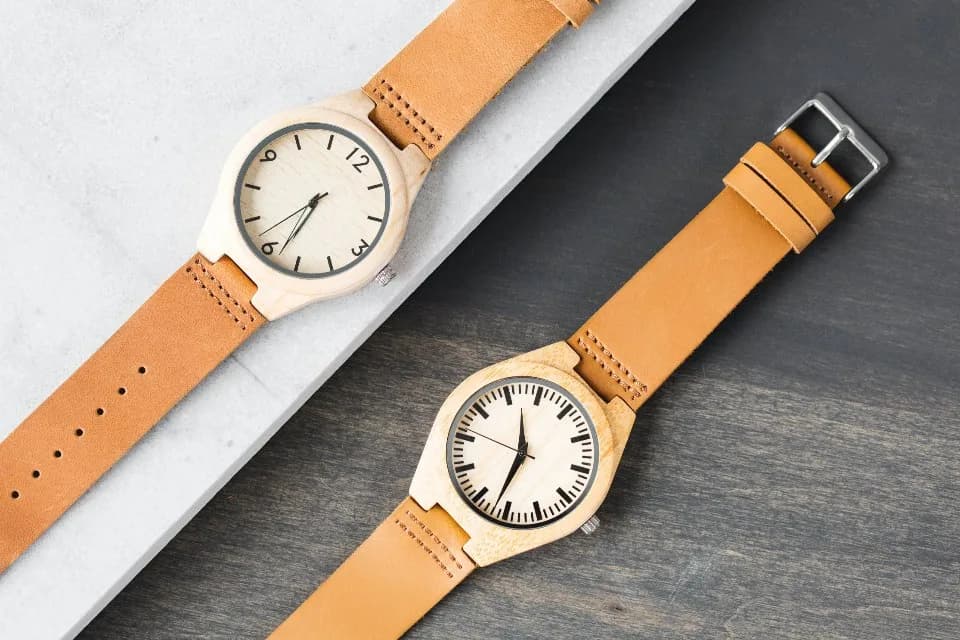 Zwei Armbanduhren mit hellem Holzgehäuse und Lederarmband, ohne erkennbare Markenaufschrift