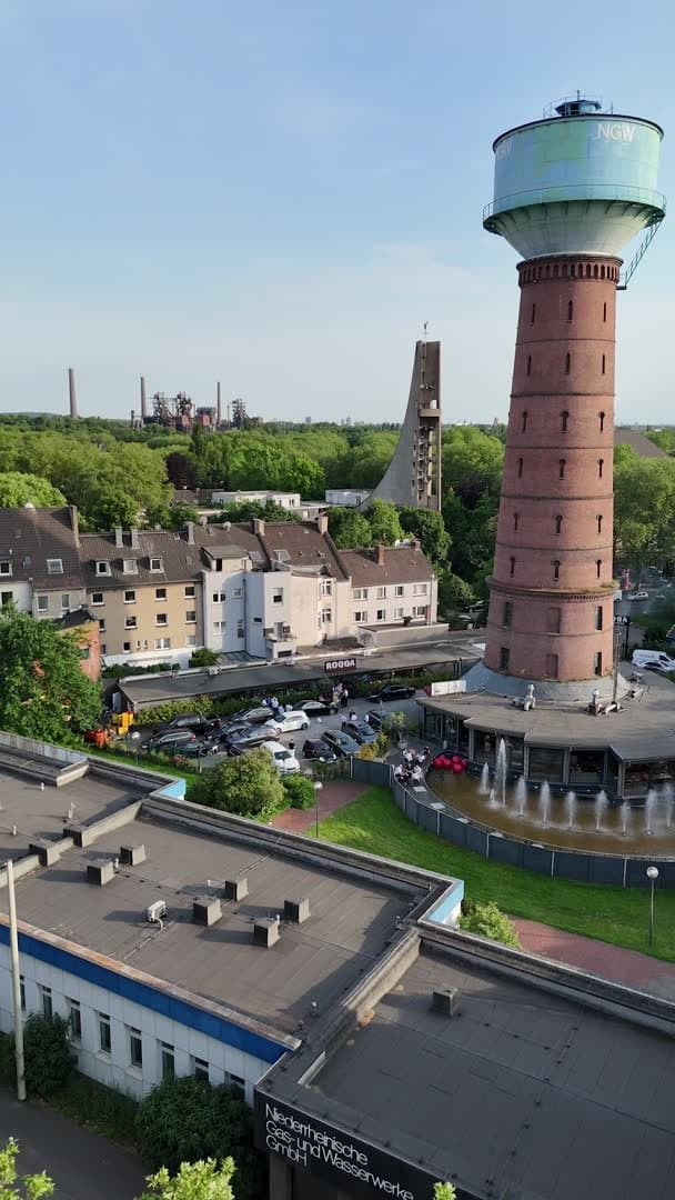 Luftaufnahme eines historischen Wasserturms mit Wohnbebauung und Industrie im Hintergrund