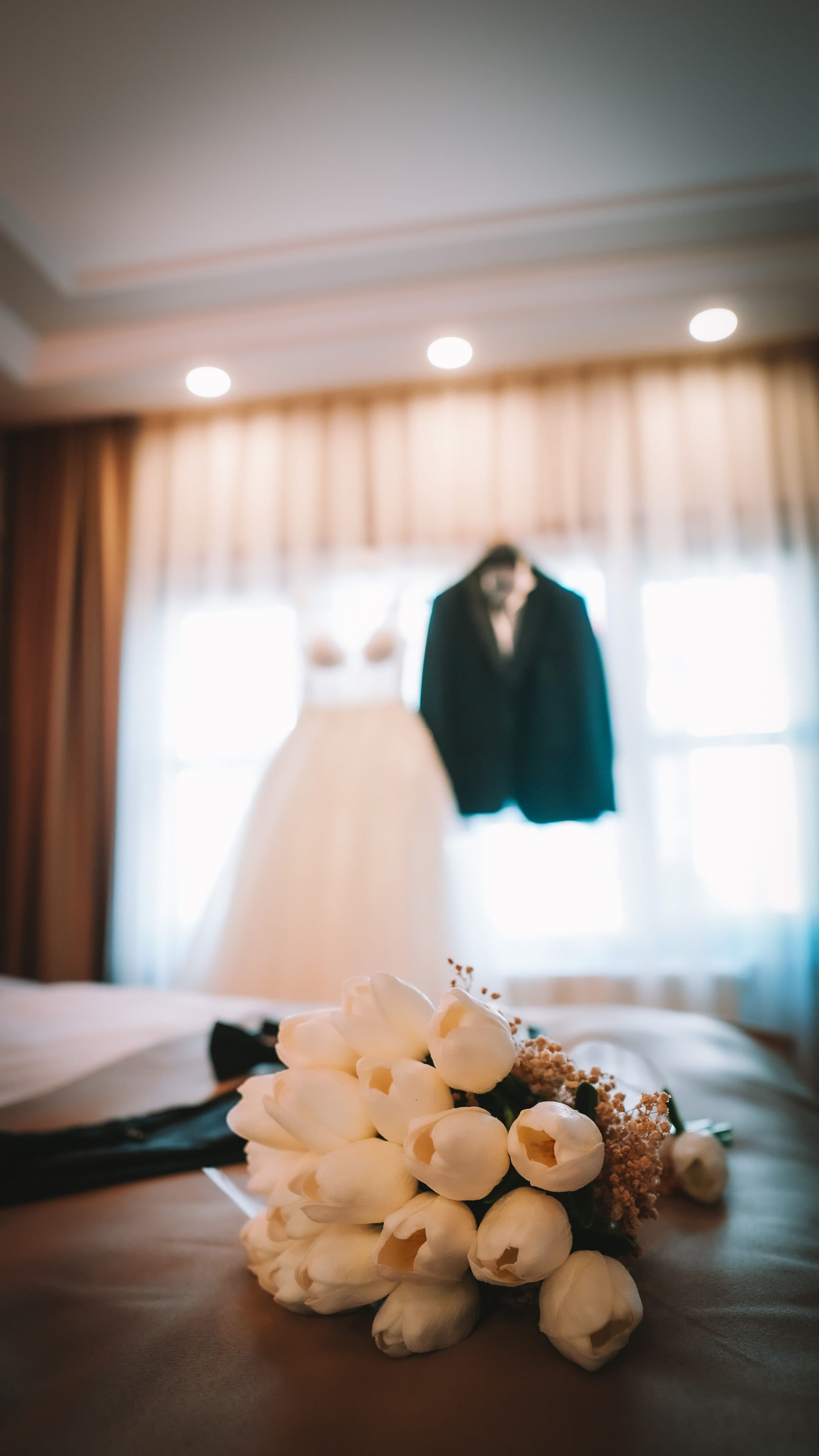 Brautkleid und Anzug des Bräutigams nebeneinander an einem Fenster